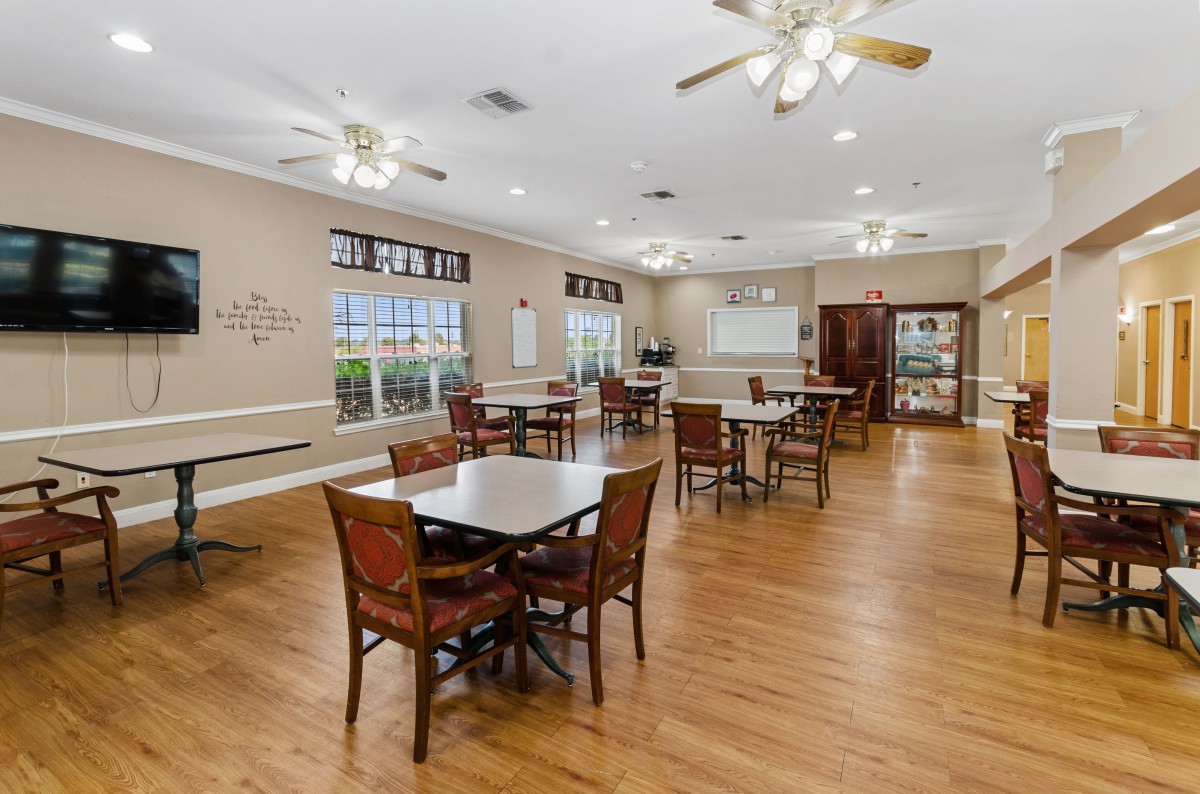 A spacious, well-lit dining area with tables and chairs, featuring wood flooring and ceiling fans.