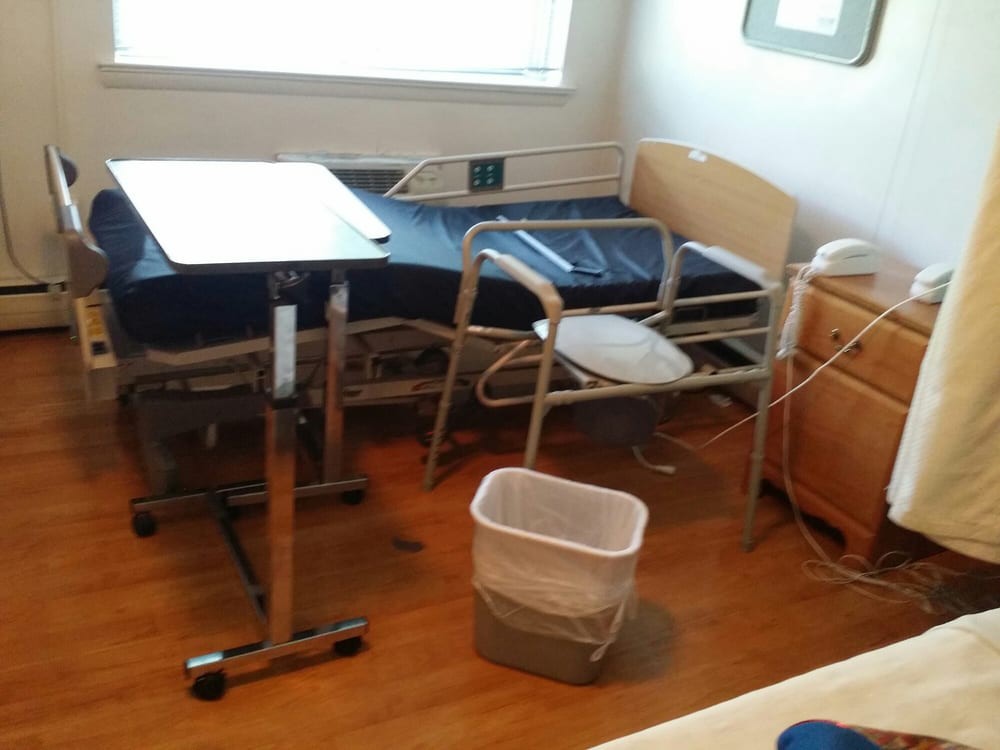 An empty hospital room with a patient bed, adjustable table, and basic medical equipment.
