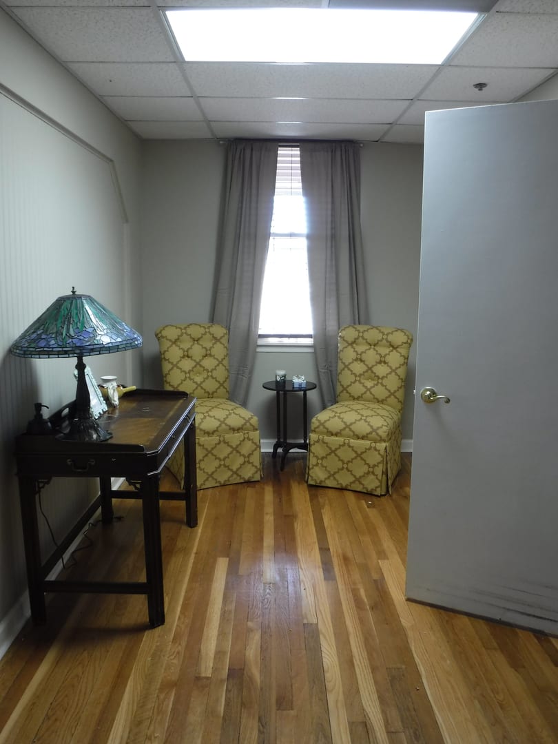 A small office space with two chairs, a desk, and a lamp near a window.