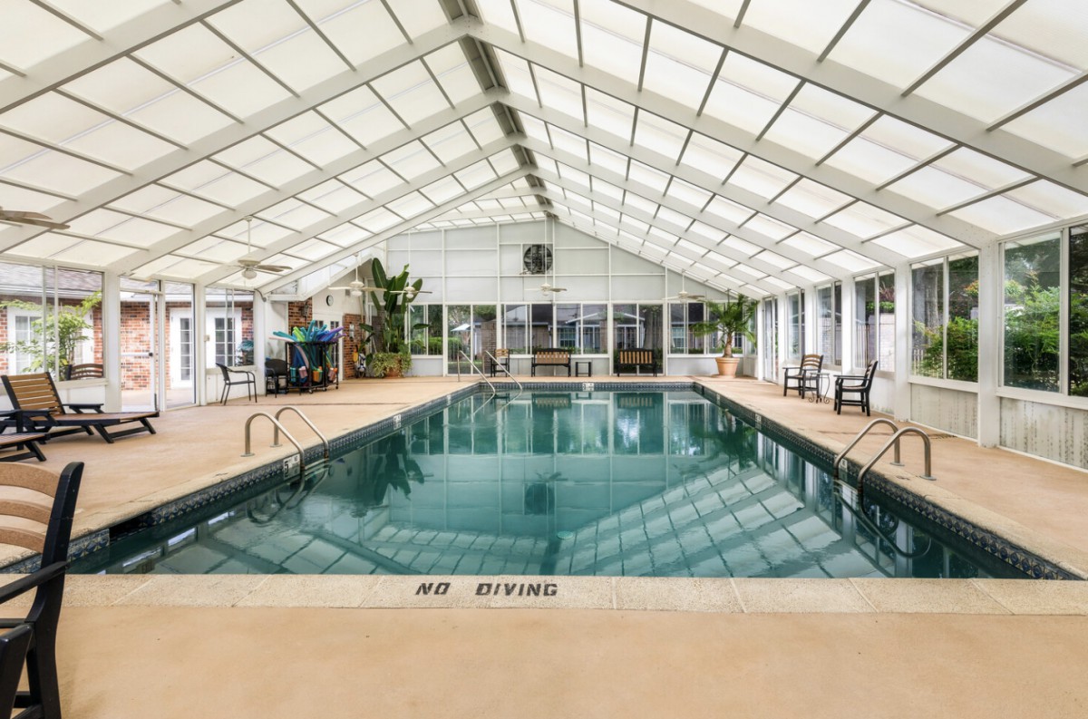 Spacious indoor swimming pool with a glass roof, surrounded by seating and plants.