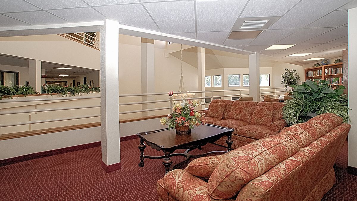A cozy living room with a patterned sofa, a coffee table, and a potted plant on red carpet flooring.