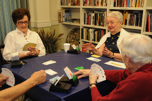 A group of elderly friends enjoying a lively card game together in a cozy library setting.