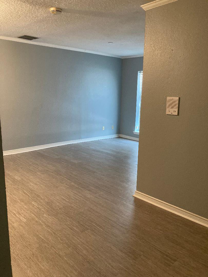 An empty room with gray walls and wood-like flooring, ready for furnishing.