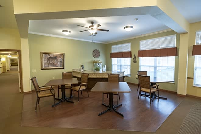 A cozy dining area with tables and chairs, featuring wood flooring and a ceiling fan.