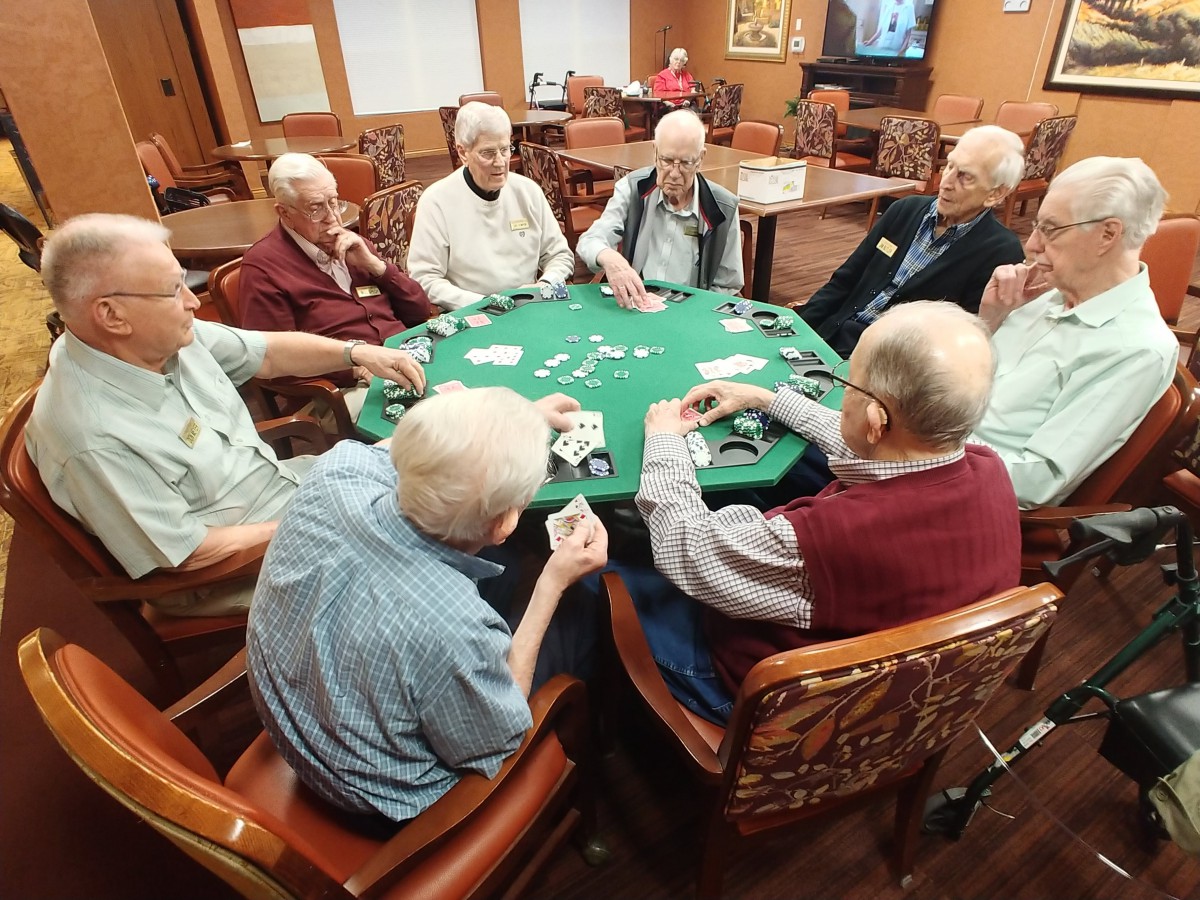 A group of seniors playing poker around a table in a cozy room.