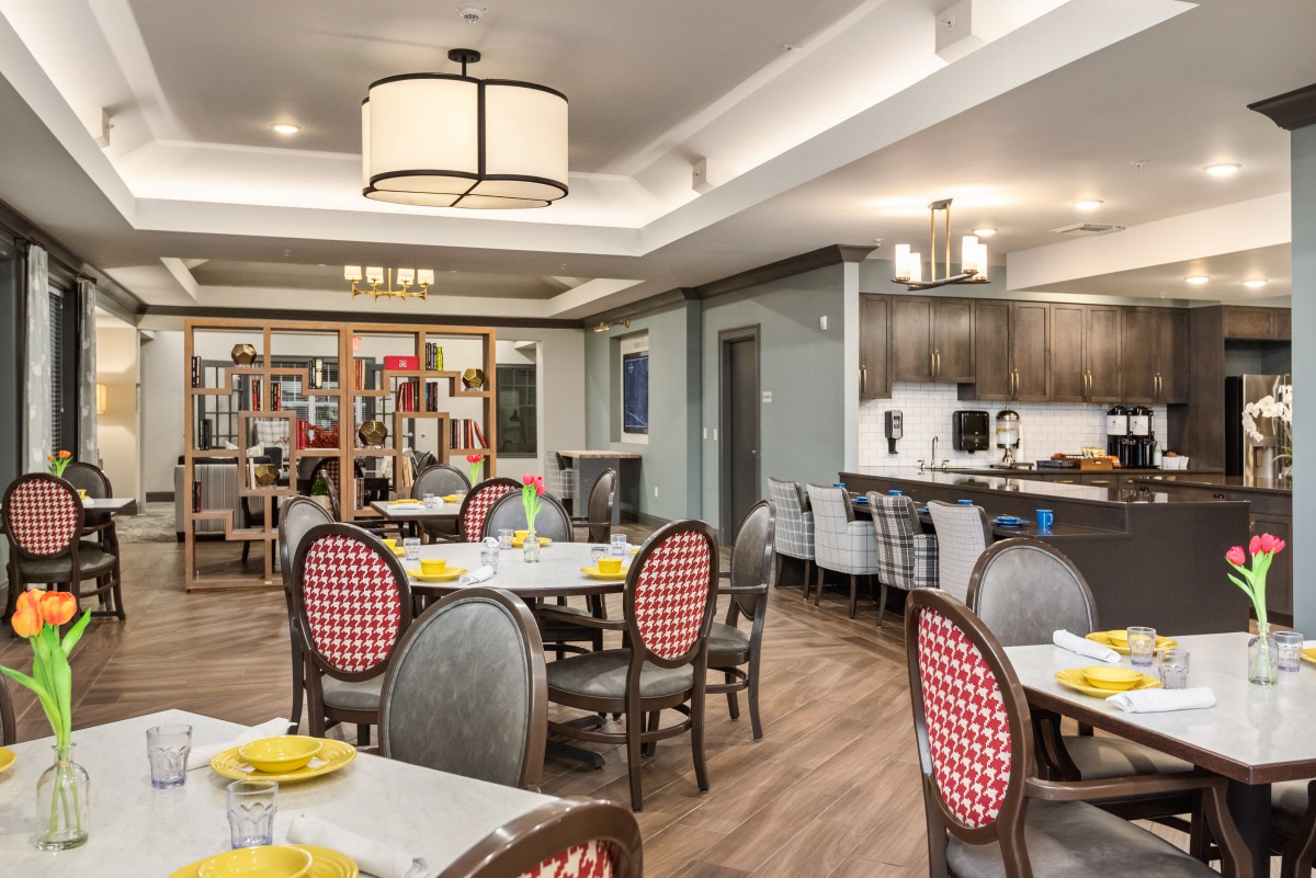 A well-furnished dining room with tables set for a meal and a kitchen area in the background.
