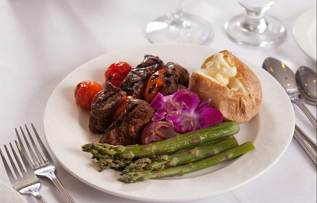 A gourmet meal featuring steak, asparagus, cherry tomatoes, and a baked potato served on a fine dining plate.