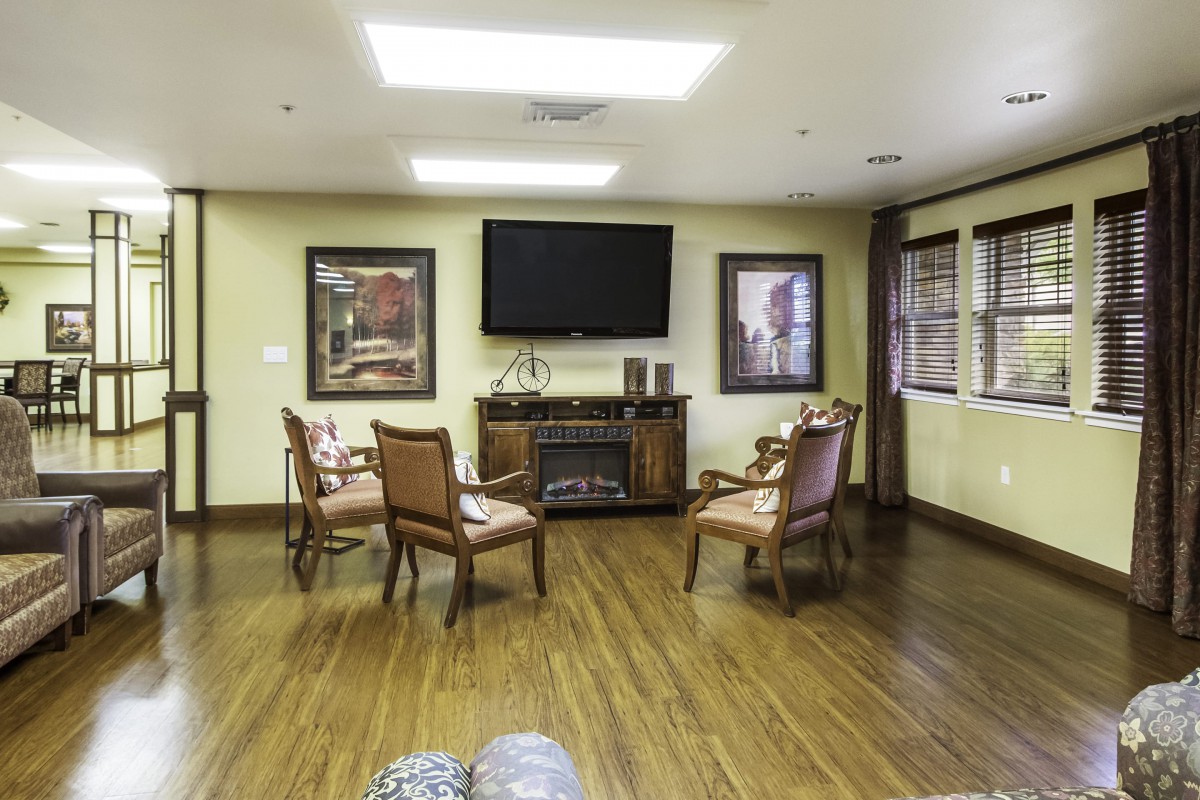 A cozy living room with wooden chairs arranged around a TV and fireplace.