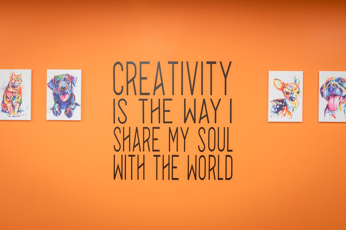 An inspiring quote about creativity on an orange wall, flanked by two pieces of art.