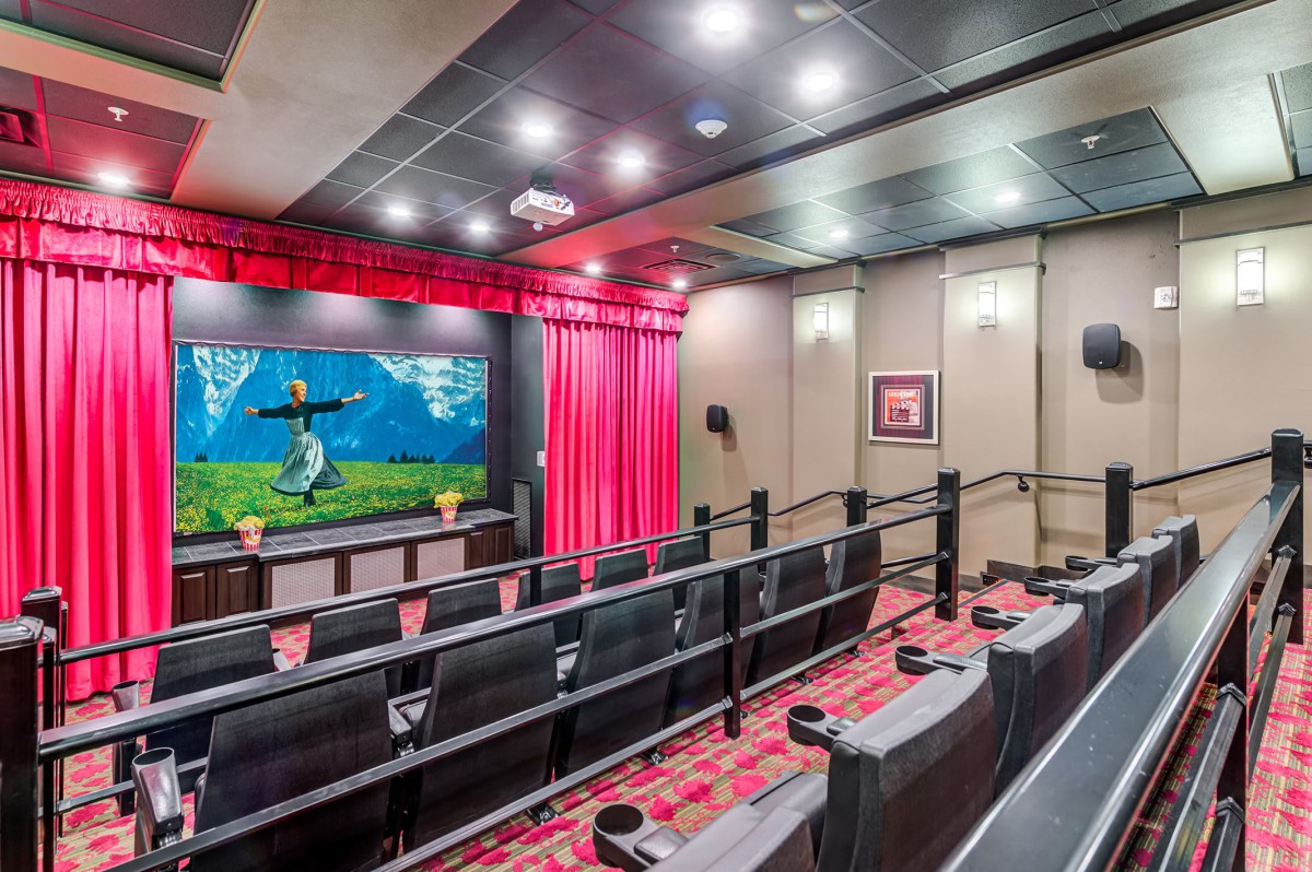 A cozy home theater setup with tiered seating, a projector screen displaying a movie scene, and ambient lighting.