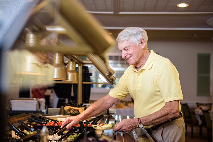 An elderly man smiles as he serves himself at a buffet in a restaurant.