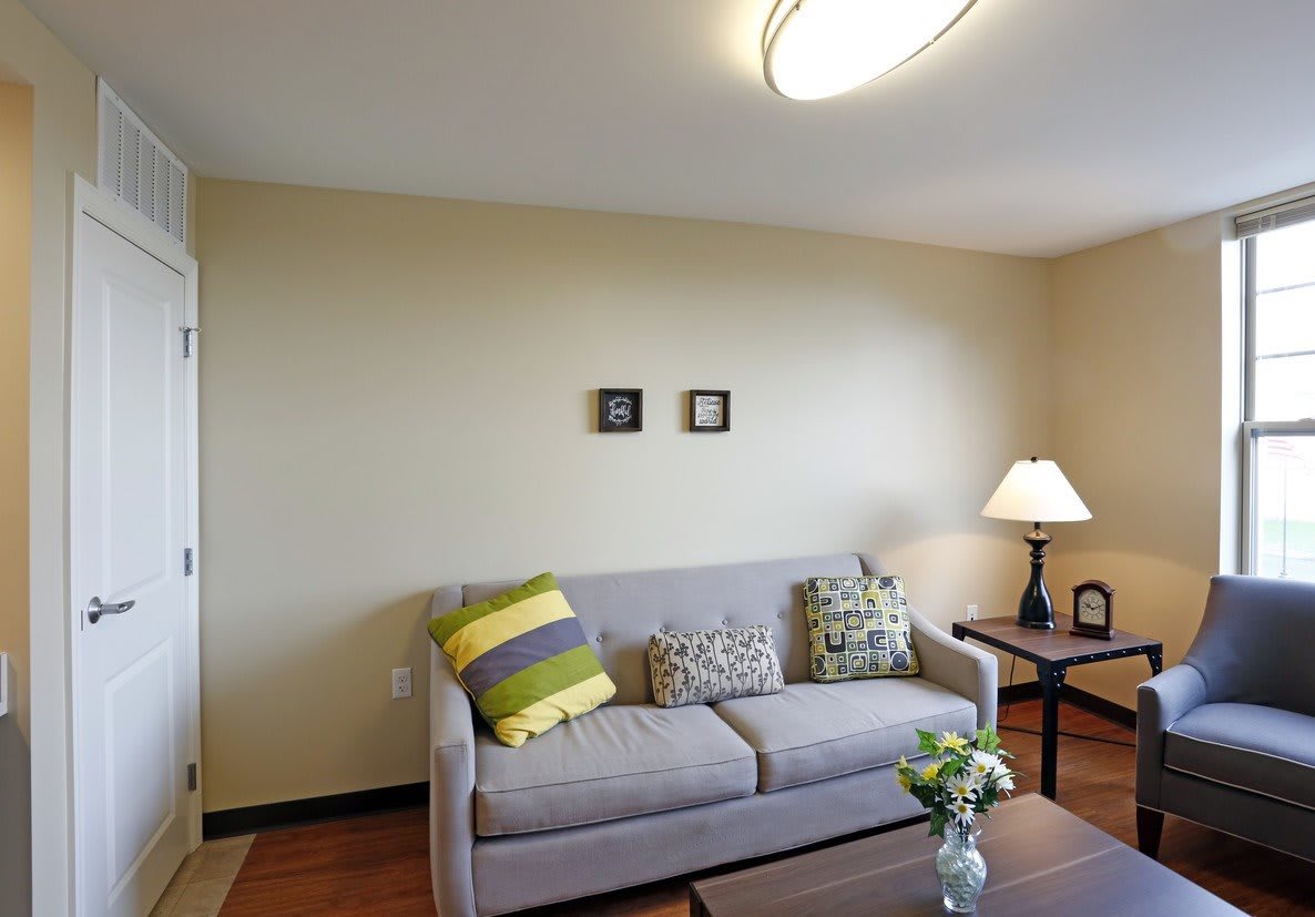 A cozy living room with a sofa adorned with colorful cushions, accompanied by a side table and lamp.