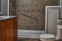 A modern bathroom featuring a toilet, sink, tiled walls, and a shower with a grab bar.