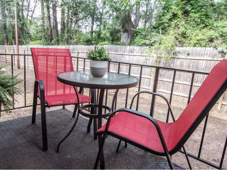 A cozy patio with red chairs and a small round table, set against a wooden fence surrounded by trees.
