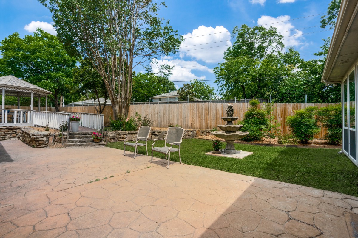 A serene backyard featuring a patio with chairs, a beautiful fountain, and lush greenery.