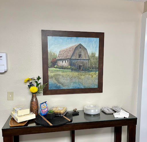A cozy interior space featuring a landscape painting of a barn, accompanied by a decorative vase with flowers.