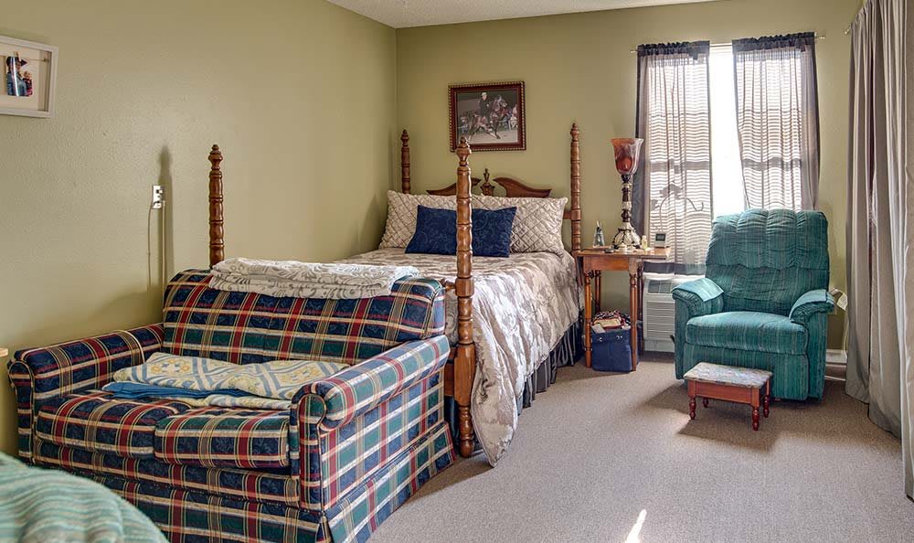 A cozy bedroom with a bed, sofa, and armchair by the window.