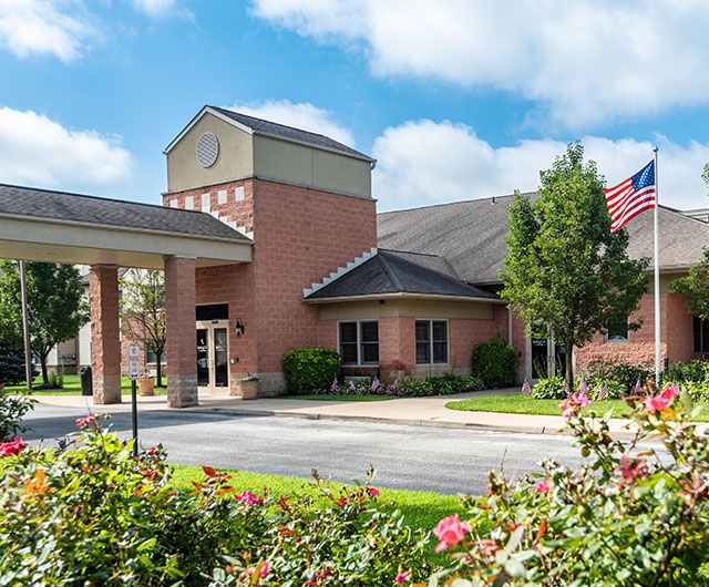 A healthcare clinic with a brick exterior and surrounding landscaping, featuring an American flag in the foreground.