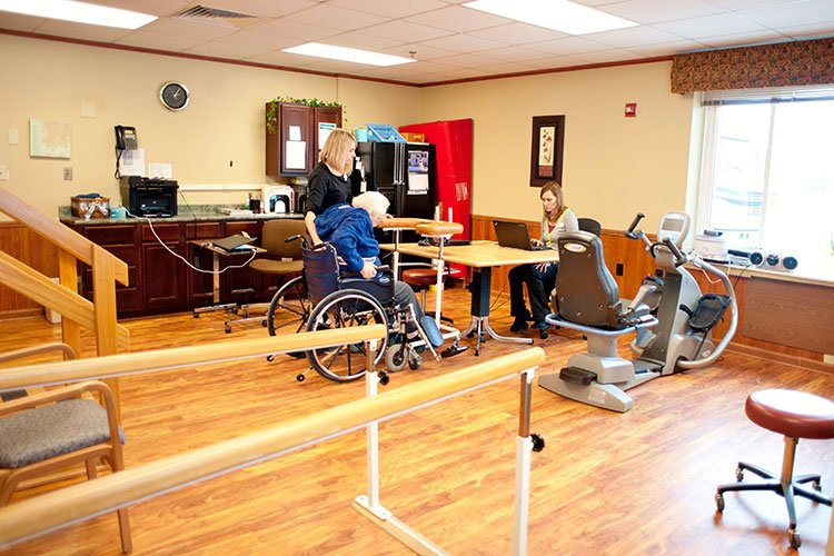 A rehabilitation room featuring exercise equipment, parallel bars, and individuals engaged in physical therapy activities.