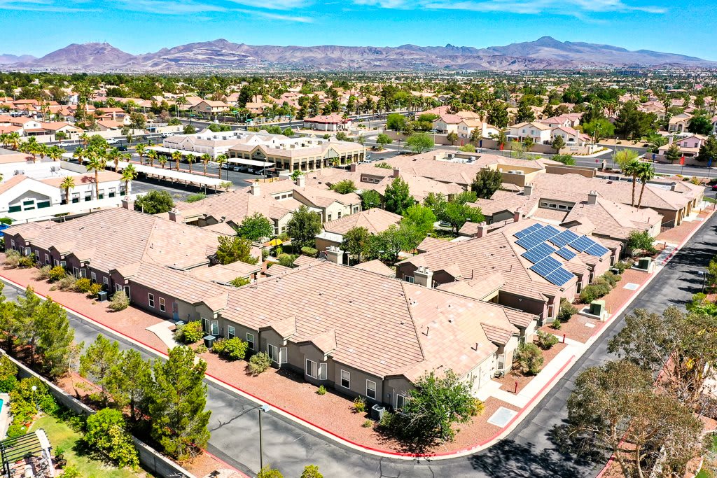 Aerial view of a suburban residential area with buildings, solar panels, and mountainous landscape in the background.