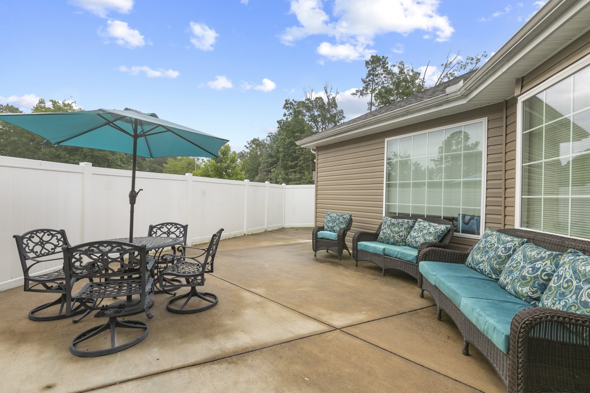 A spacious patio with outdoor furniture and an umbrella, set against a sunny backyard.