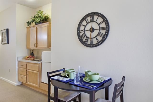 A cozy kitchen with a small dining table set for two, featuring a stylish wall clock and modern decor.
