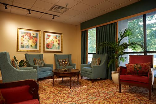 A cozy living room with blue chairs, a wooden coffee table, vibrant artwork on the walls, and a large potted plant.