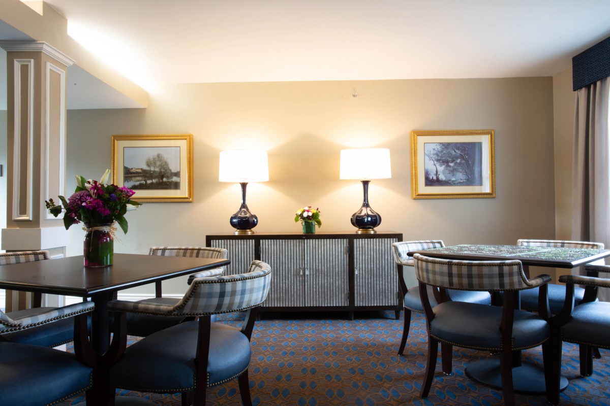 A well-lit dining room with chairs, a central table, two lamps, and framed artwork on the walls.