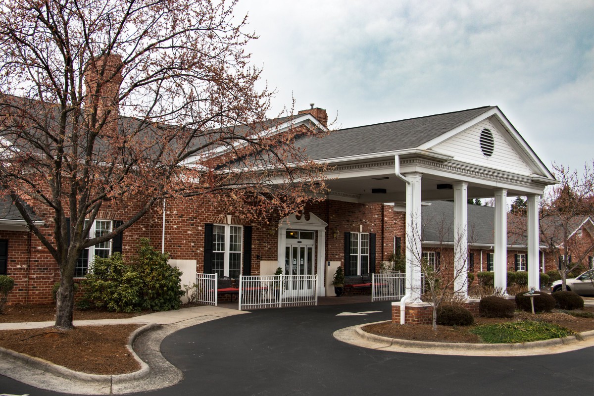 A welcoming entrance of a brick building with a covered driveway and surrounding trees.