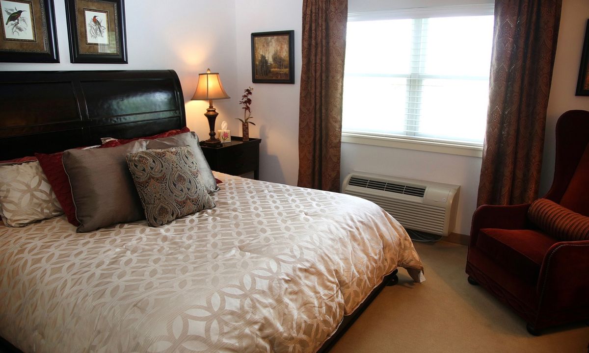A cozy bedroom featuring a neatly made bed with decorative pillows, a bedside lamp, and framed artwork on the wall.
