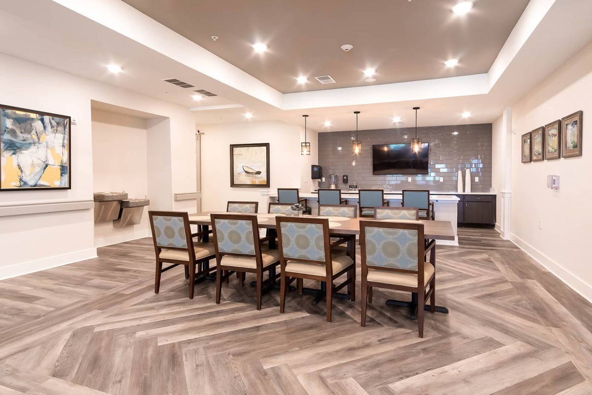 A modern dining room featuring a large table, stylish chairs, and herringbone flooring, complete with a bar area and television.