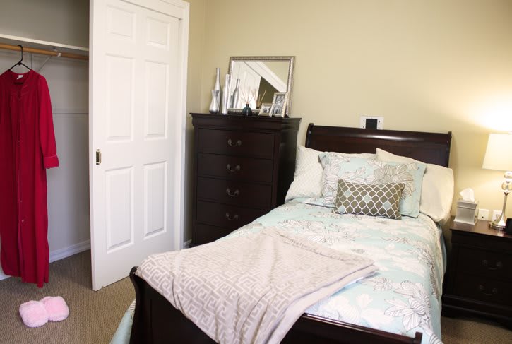 A cozy bedroom with a neatly made bed and a dresser with a mirror.