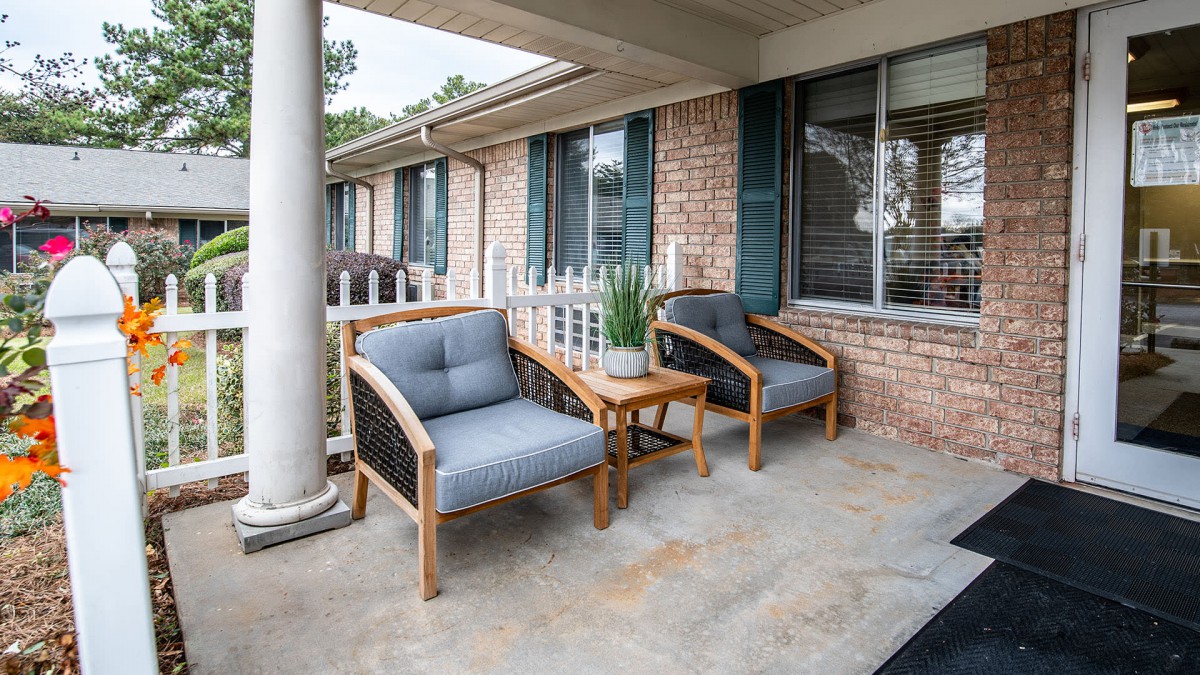 A cozy patio setup with two cushioned chairs and a small table with a plant, set against a brick wall with windows.