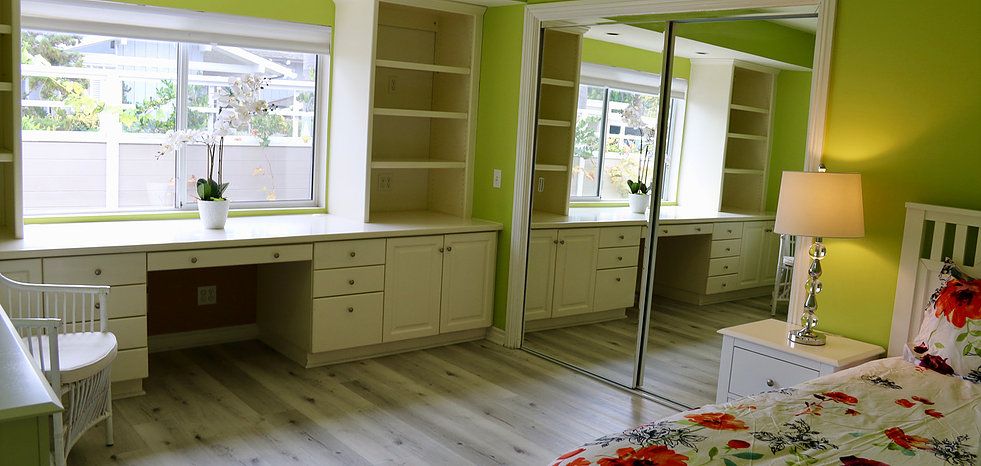 A bright room with built-in desks and shelves, large mirrored closet doors, and green walls.