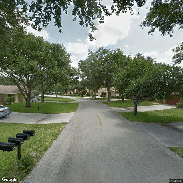 A quiet suburban street lined with trees and houses, featuring mailboxes and driveways.