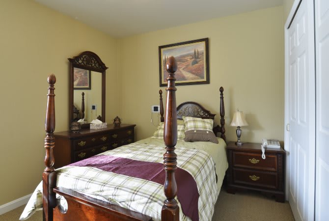 A cozy bedroom featuring a single bed with a wooden frame, matching dresser and mirror, and elegant decor.