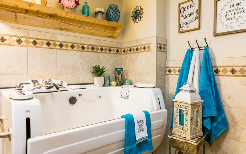 A cozy bathroom featuring a white bathtub adorned with turquoise towels, decorative plants, and wall accents.