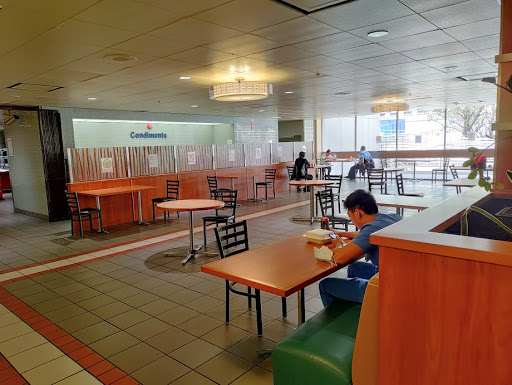 A spacious cafeteria with tables and chairs, featuring a few individuals dining.