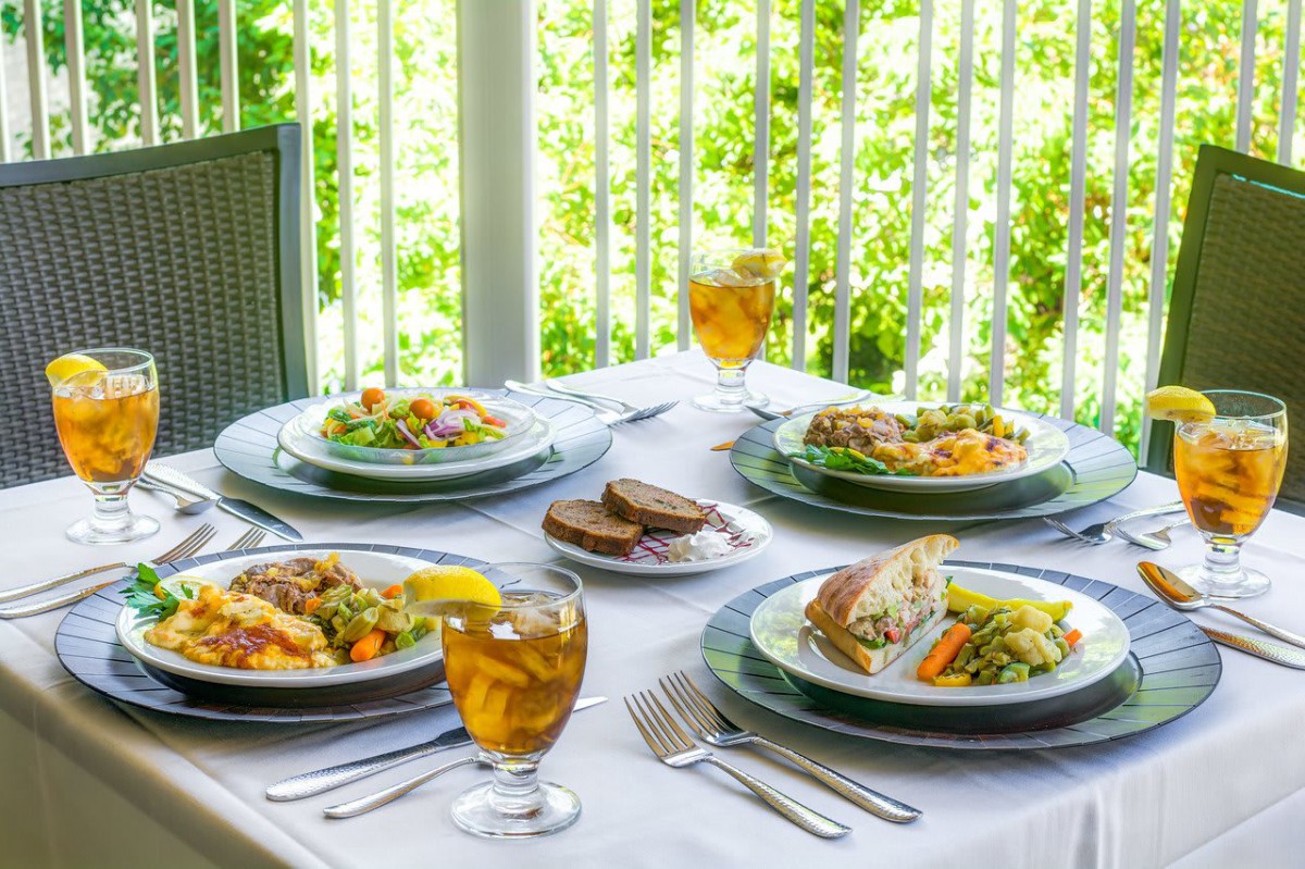 A beautifully set outdoor table with plates of salad and glasses of iced tea.