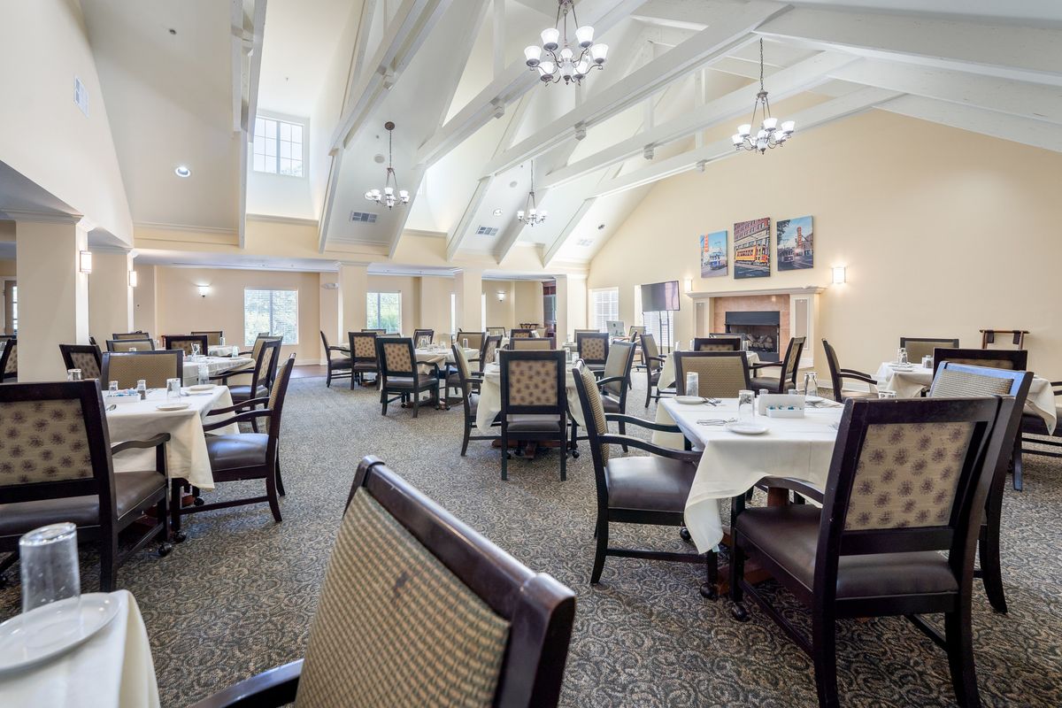 A spacious and elegantly decorated dining room with neatly arranged tables and chairs under a bright ceiling with chandeliers.