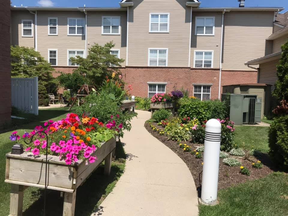 A vibrant garden with a variety of flowers along a winding pathway beside a residential building.
