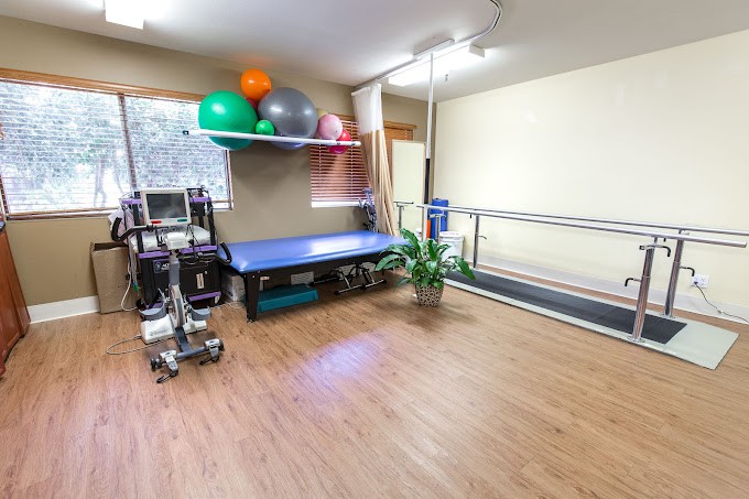 A well-equipped physical therapy room with parallel bars, exercise balls, and a treatment table.