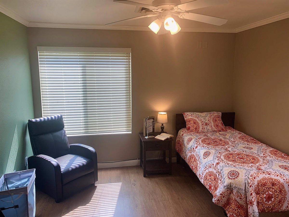 A cozy bedroom with a single bed and recliner chair under soft lighting.
