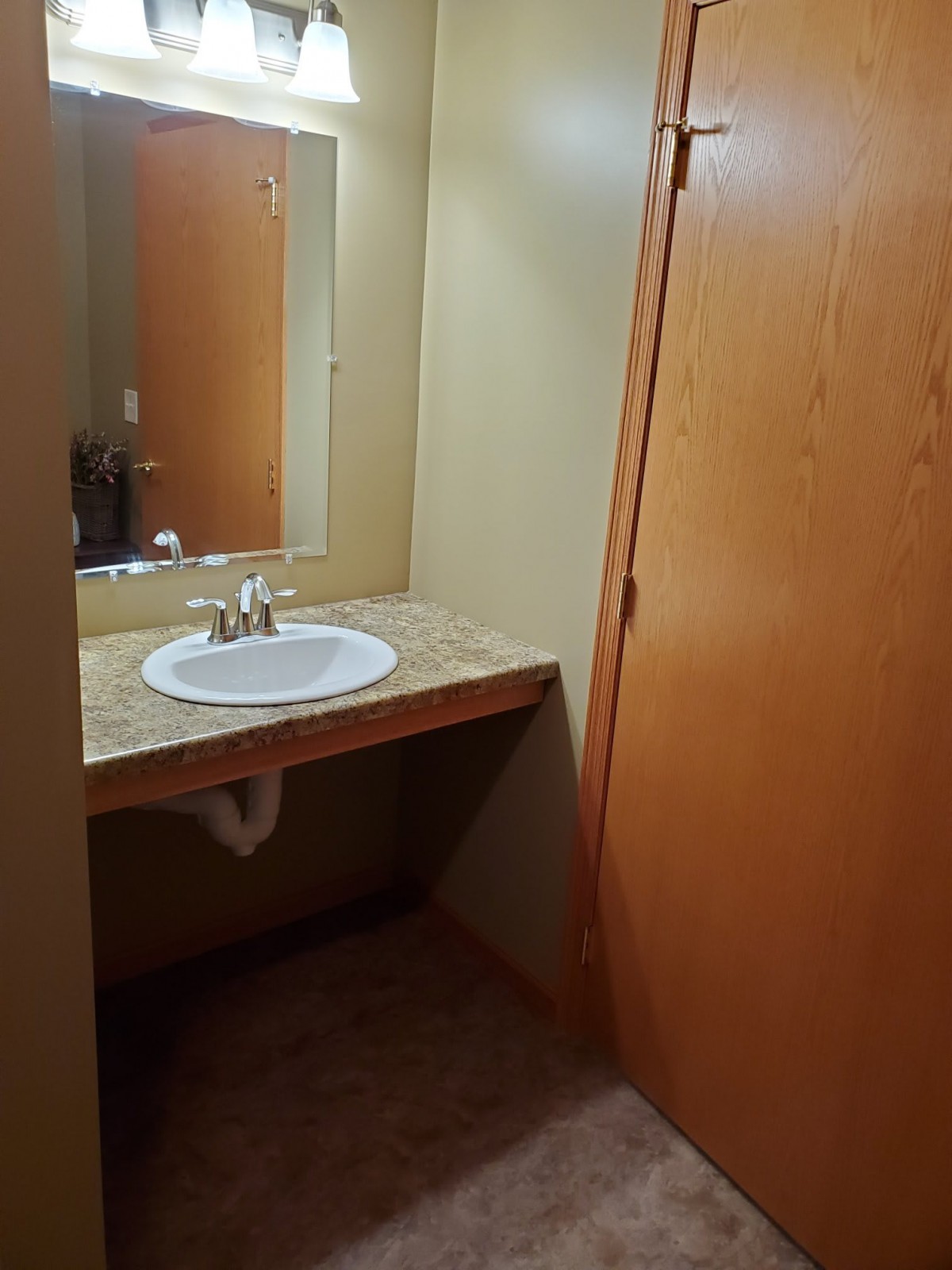 A compact bathroom with a sink and mirror next to a wooden door.