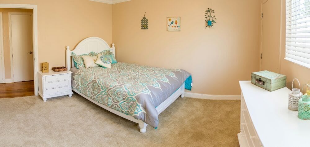 A cozy bedroom with a neatly made bed and decorative wall hangings.