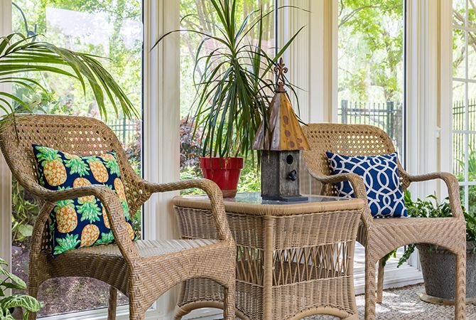 A cozy sunroom with wicker furniture, adorned with decorative pillows and surrounded by lush indoor plants.