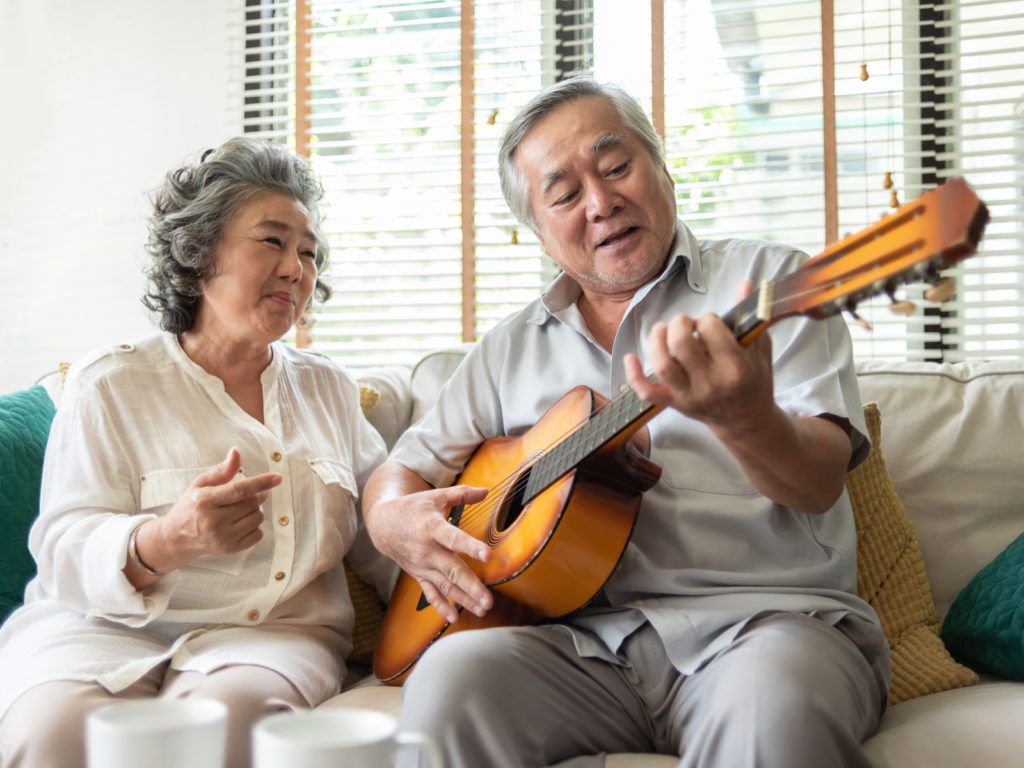 An elderly couple enjoying a musical moment together as the man plays the guitar in their cozy living room.