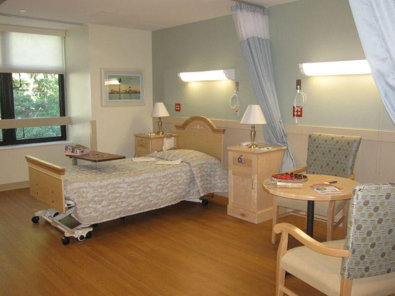 A well-lit hospital room with a single bed and comfortable seating.