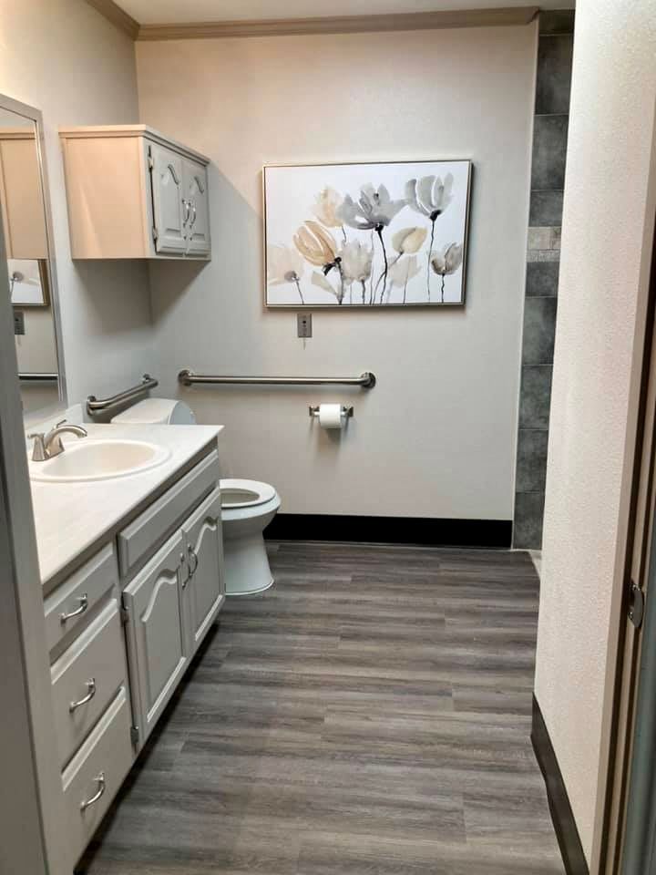 A modern bathroom with a white sink, toilet, and floral artwork on the wall.