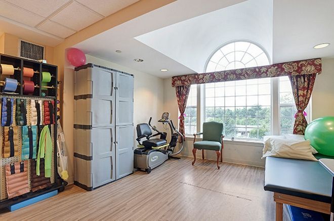 A well-lit room featuring exercise equipment, a large window, and wooden flooring.